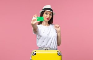 Homepage 8 Mulher jovem segurando um cartão de crédito verde ao lado de uma mala amarela, simbolizando planejamento financeiro para viajar e acumular milhas com praticidade e estilo.