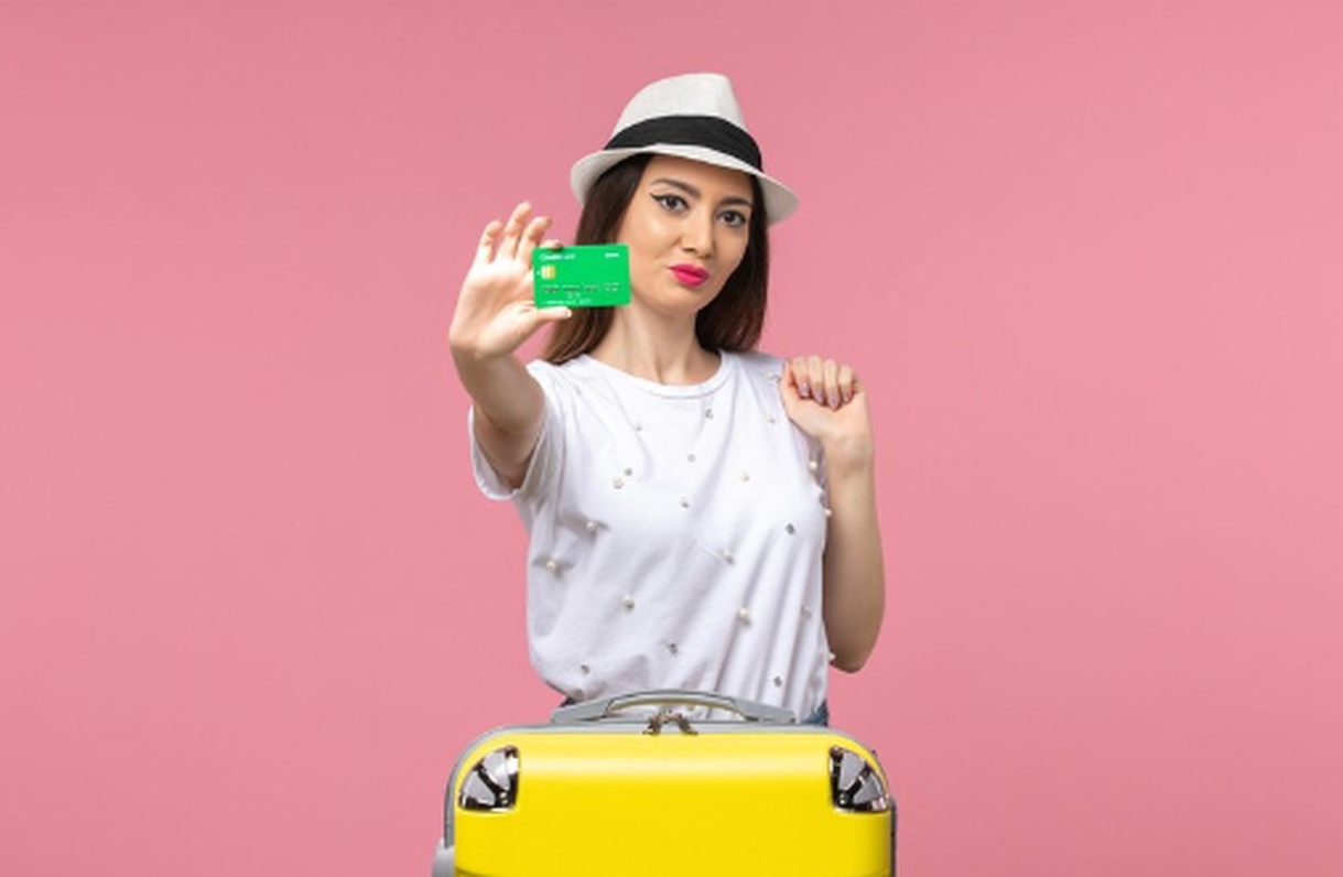 Mulher jovem segurando um cartão de crédito verde ao lado de uma mala amarela, simbolizando planejamento financeiro para viajar e acumular milhas com praticidade e estilo.