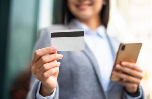 New Home 36 Mulher sorridente segura um smartphone e um cartão de crédito, representando praticidade e modernidade na escolha de cartões sem anuidade com benefícios premium.