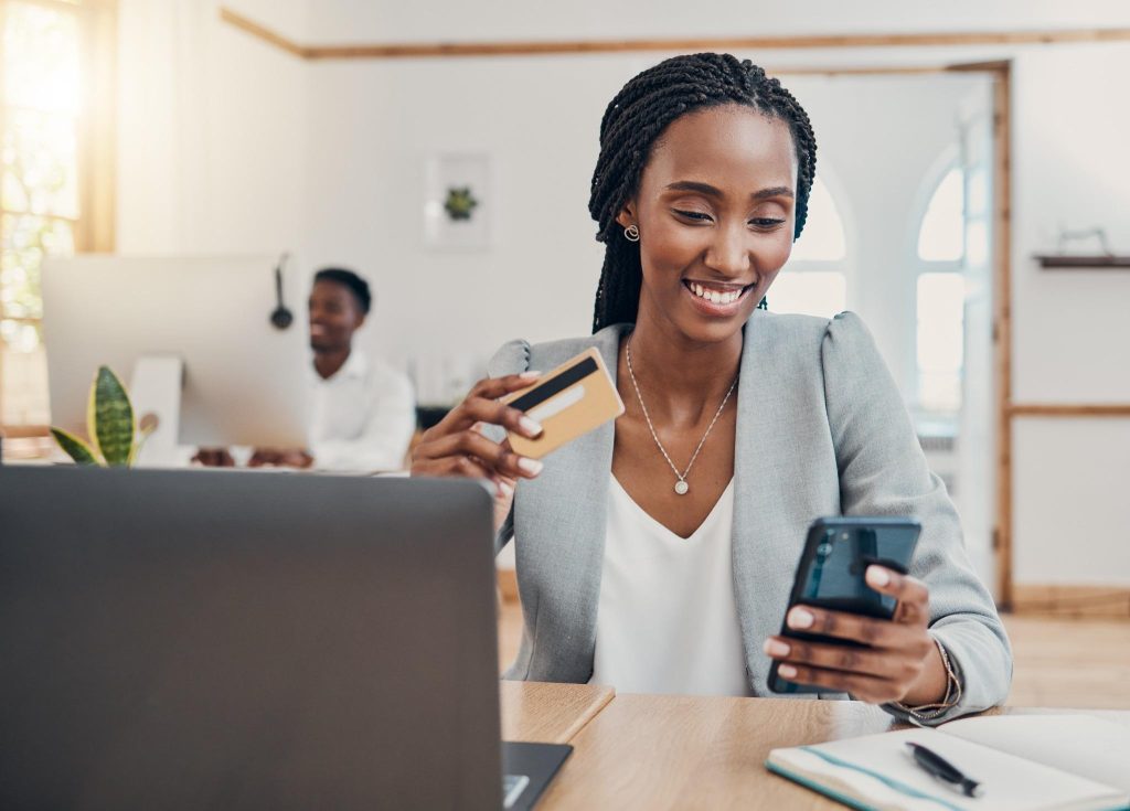 Como aumentar o score de crédito: hábitos que funcionam de verdade 1 Mulher sorridente usando cartão e celular após aumentar score de crédito
