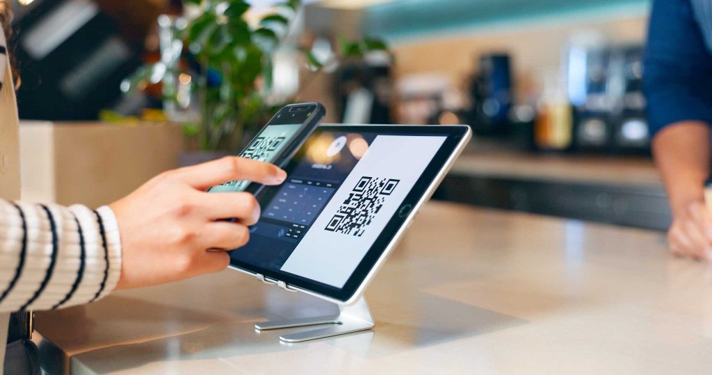 Como escolher um banco digital: critérios, comparação e cuidados de segurança 1 Pessoa usando celular para pagar com QR Code em loja — exemplo de como escolher um banco digital com praticidade.