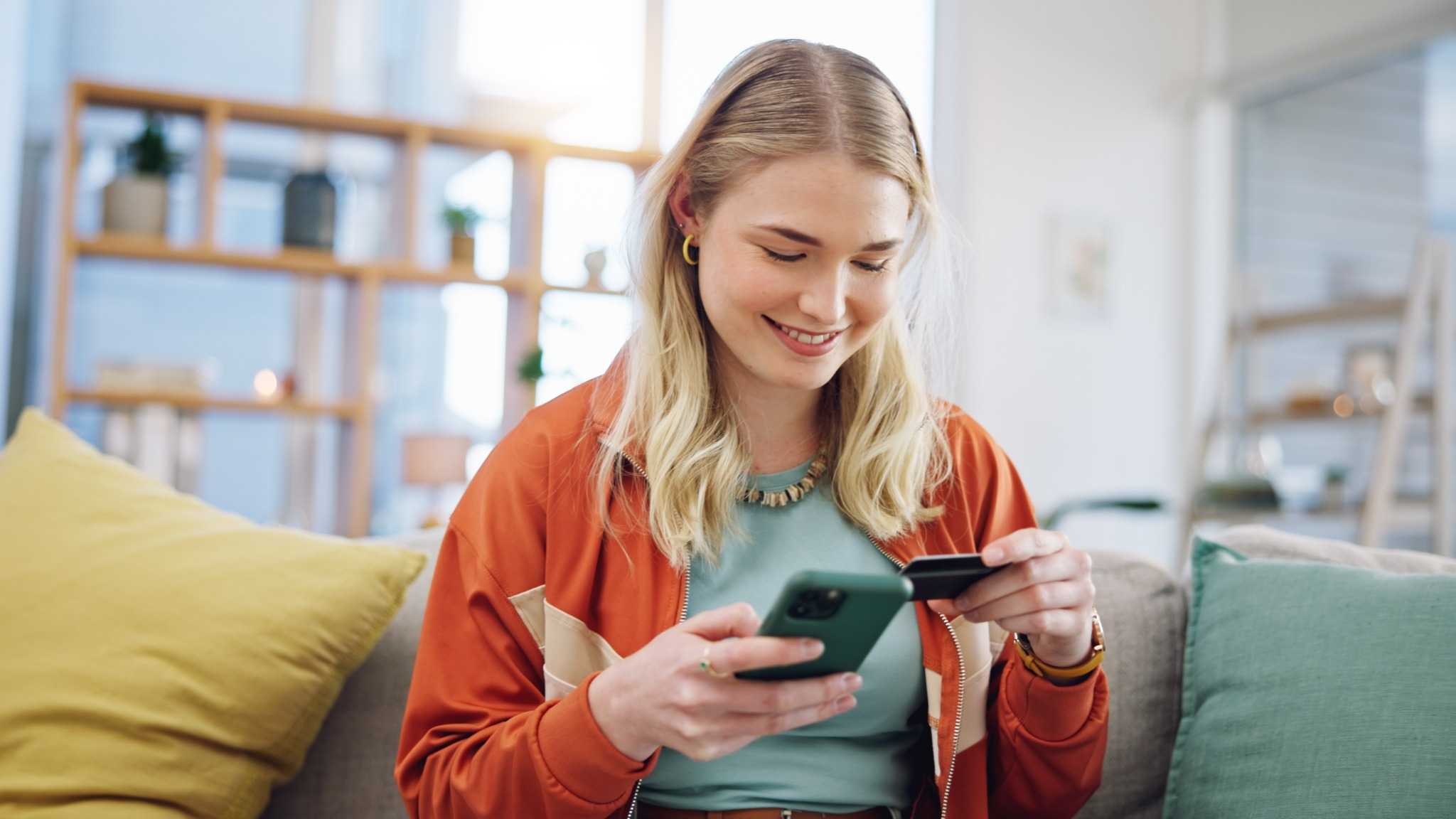 Mulher usando celular e cartão em casa — ilustração de como escolher um banco digital com segurança e conveniência.