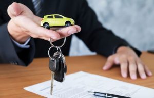 Pessoa segurando chaves de veículo e um carrinho em miniatura sobre um contrato, representando a assinatura de financiamento de carro.