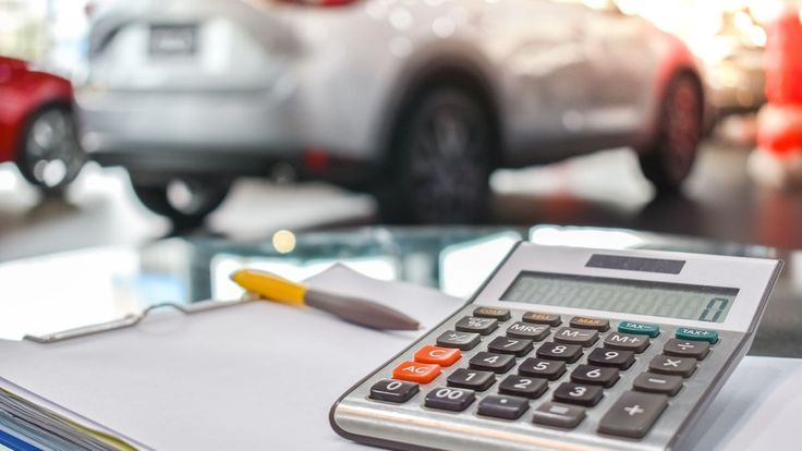 Calculadora e contrato sobre a mesa em concessionária, simbolizando o cálculo de parcelas em um financiamento de carro.