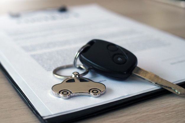 Chave de carro com chaveiro em formato de automóvel sobre contrato, representando a assinatura de financiamento de carro.