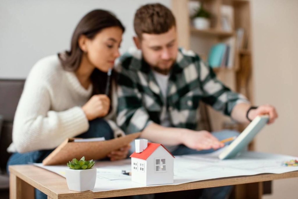 Casal analisando documentos financeiros em casa, com miniatura de imóvel sobre a mesa, representando o uso de bens como garantia em um empréstimo para negativado.