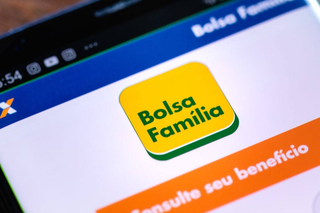 Tela de celular exibindo o aplicativo oficial do Bolsa Família, com o logotipo em destaque em fundo amarelo e verde. Abaixo aparece a opção “Consulte seu benefício”. O layout pertence ao app da Caixa Econômica Federal.