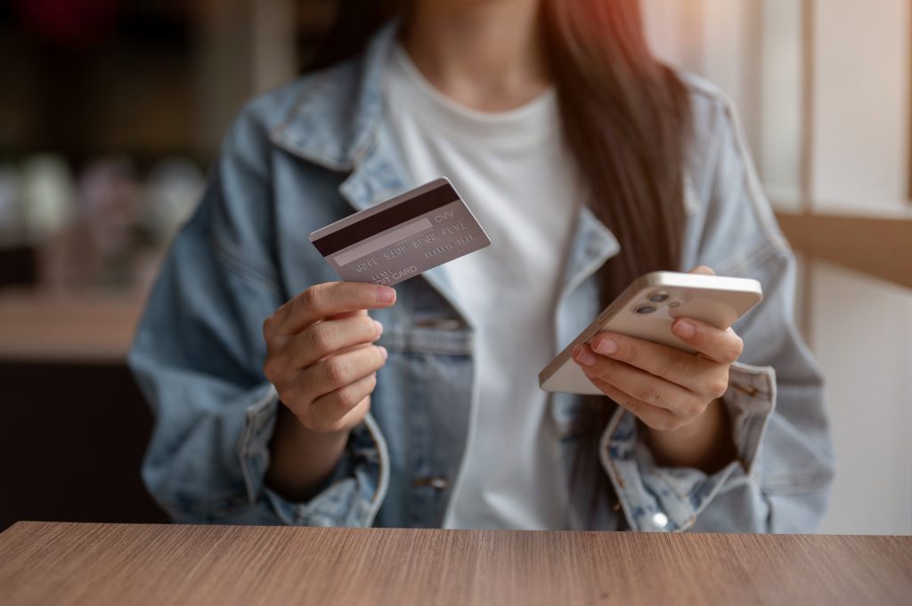 Como aumentar o limite do cartão de crédito com segurança 1 “Mulher segurando cartão e celular enquanto consulta app bancário para aumentar limite cartão de crédito”