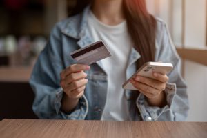 “Mulher segurando cartão e celular enquanto consulta app bancário para aumentar o limite do cartão de crédito”