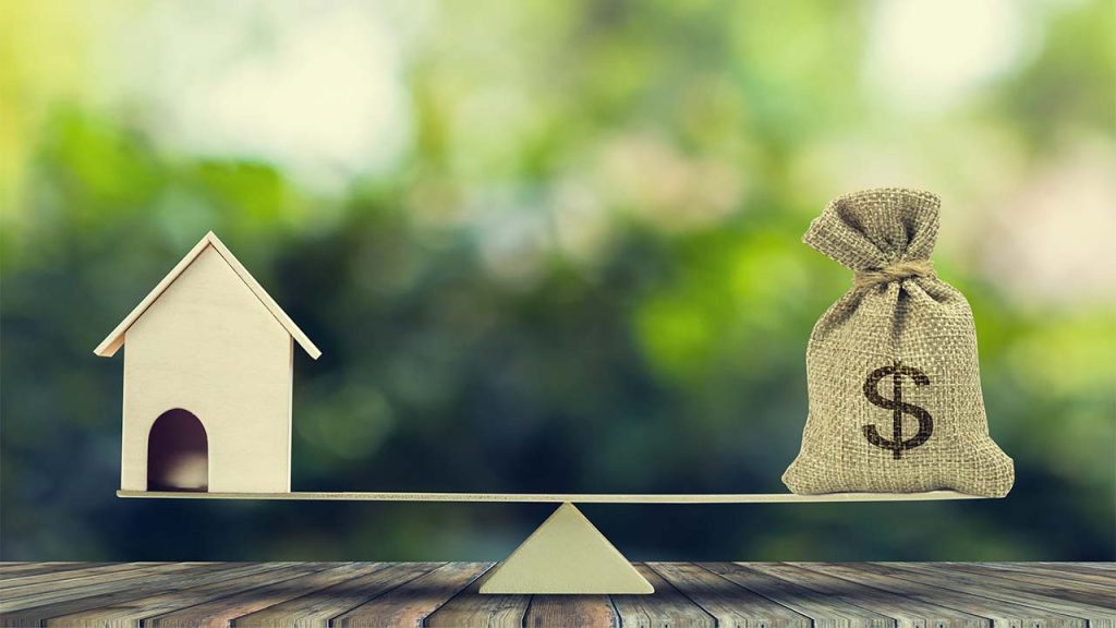 Empréstimo com garantia: como funciona, taxas e cuidados antes de contratar? 1 Imagem representando um empréstimo financeiro: um saco de dinheiro com a palavra ‘LOAN’ equilibrado em uma balança com recortes de uma casa, carro e família, simbolizando crédito com garantia e estabilidade financeira