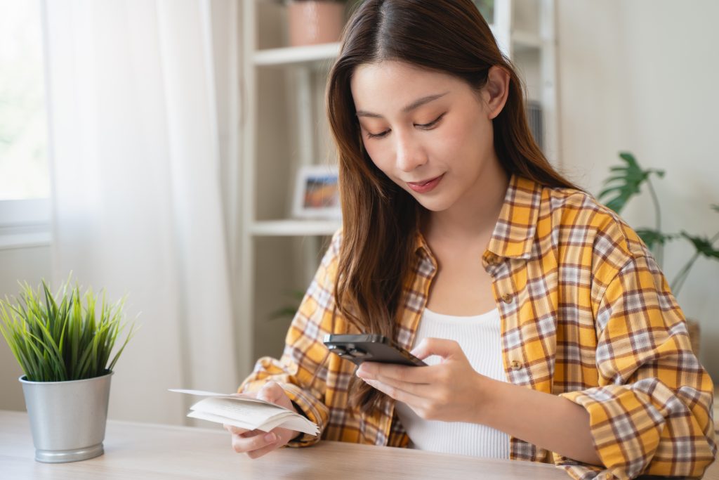 Conta digital que rende mais que a poupança: melhores opções em 2025 1 Mulher usando o celular e segurando comprovantes para controlar suas finanças e escolher uma conta digital que rende mais que a poupança.