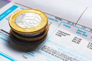 Moedas de um real sobre uma conta de luz, ilustrando informações sobre Crefaz empréstimo na conta de luz e serviços financeiros vinculados à fatura.