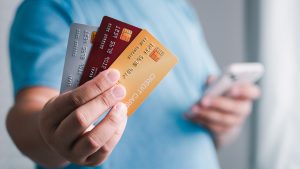 Pessoa segurando vários cartões enquanto usa o celular, ilustrando diferentes opções de cartão de crédito alta renda voltadas para consumidores com maior poder aquisitivo.