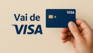 Cartão Visa azul sendo segurado por uma mão sobre fundo claro, com destaque para o chip e o símbolo de pagamento por aproximação, acompanhado do texto Vai de Visa, representando benefícios e vantagens do programa Vai de Visa em pagamentos com cartão Visa.