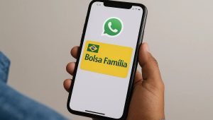 Imagem mostrando uma mão segurando um smartphone cuja tela exibe os logotipos do WhatsApp e do programa Bolsa Família. A interface do aparelho está clara e nítida, destacando o ícone verde do WhatsApp na parte superior e o cartão amarelo do Bolsa Família com a bandeira do Brasil no canto esquerdo. A cena sugere comunicação ou consulta de informações pelo aplicativo, remetendo ao tema Empréstimo Bolsa Família pelo WhatsApp.