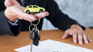 Pessoa segurando chaves de veículo e um carrinho em miniatura sobre um contrato, representando a assinatura de financiamento de carro.