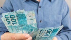 Homem segurando notas de 100 reais nas mãos representando dinheiro recebido pela venda de férias no abono pecuniário