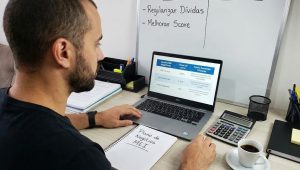 Empreendedor analisa planilha no notebook para buscar empréstimo para MEI negativado no escritório.