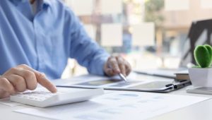 Pessoa usando calculadora e analisando documentos financeiros relacionados ao informe de rendimentos em ambiente de trabalho