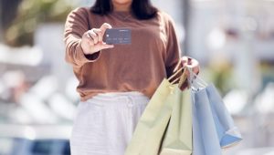 Mulher segurando sacolas de compras e exibindo um cartão de crédito, representando vantagens do cartão de crédito com cashback sem anuidade.