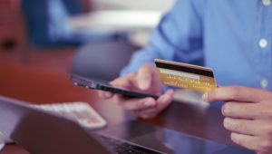Pessoa segurando cartão de crédito e usando o celular, representando o passo a passo de como cancelar compra no cartão de crédito.